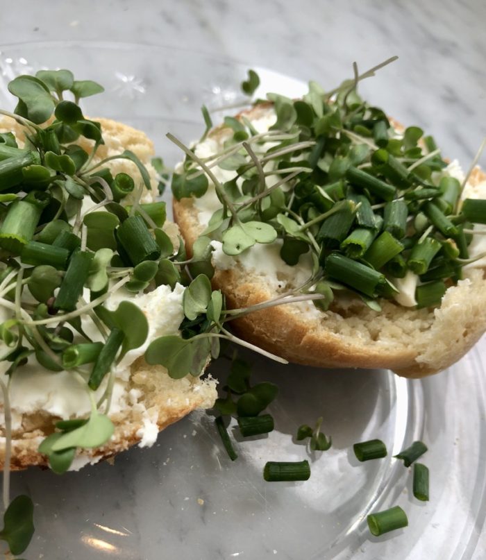 Open homemade oven-baked English muffin with cream cheese, microgreens, and fresh chives